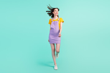 Full length photo of pretty charming young woman look empty space walk wind blow hair isolated on teal color background