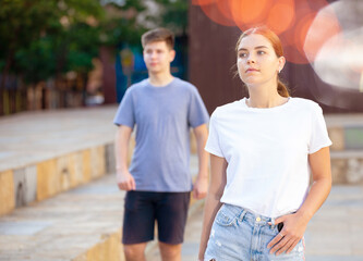 Young girl is standing and guy is walking behind her