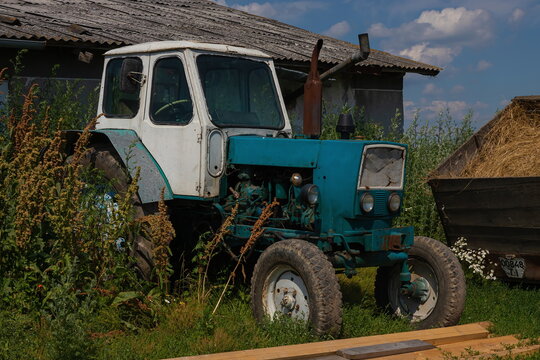 old tractor on a farm in the grass under the wall. blue sky, summer.
