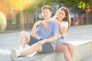 Girl is sitting with young man and hugging him from behind