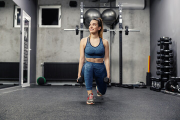Fototapeta na wymiar Steps with dumbbells to burn the muscles of the buttocks and legs. A portrait of a beautiful woman in sportswear and in good physical shape doing squats in an isolated indoor gym. Sports life
