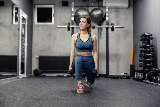 Steps with dumbbells to burn the muscles of the buttocks and legs. A portrait of a beautiful woman in sportswear and in good physical shape doing squats in an isolated indoor gym. Sports life