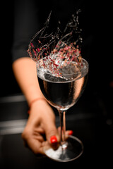 woman's hand holds glass with liquid decorated with caramel strands with flower petals