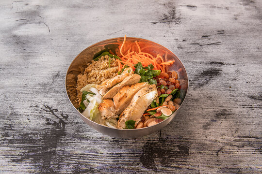 Metal bowl with roasted chicken breast chopped with quinoa, raisins, almonds and grated carrots, parsley and coriander on iceberg lettuce.