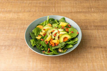 Vegan salad of spinach, avocado, chopped pineapple, nuts and peach chunks