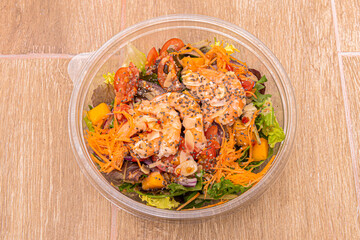Cooked prawn salad with lettuce sprouts, fried almond slices, cherry tomatoes, carrots, mango pieces in a plastic bowl for home delivery