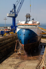 Workmen cleaning the hull of a merchant ship in the dry dock of a shipyard in Gibraltar. Cranes,...