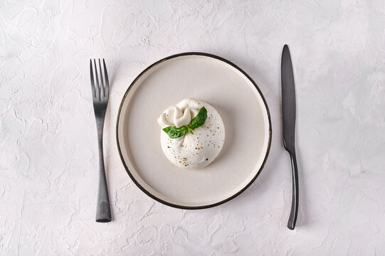 Italian cheese burrata with basil on white plate with black fork and knife. Top view. Copy space