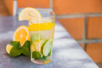 Cool freshly made lemonade in glass on white table. Lemonade with lemon, lime and ice cubes in glass. 