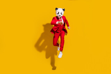 Photo of anonymous panda guy jump run look watch late wear mask red tux shoes isolated on yellow...