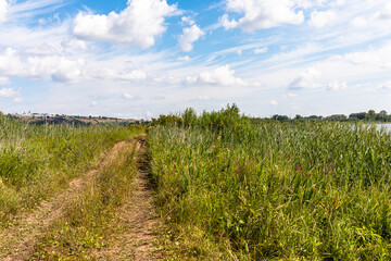 Fototapeta na wymiar On a sunny summer day, a field road runs along a small lake, the city of Yelabuga, Tatarstan, Russia is visible on the horizon on a high hill on the left.