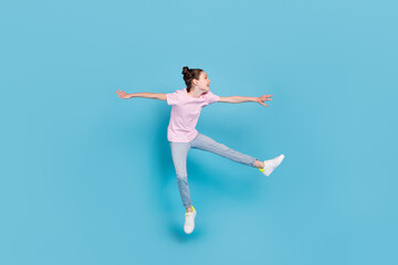 Photo of sweet funny schoolgirl dressed pink t-shirt jumping high looking empty space smiling isolated blue color background