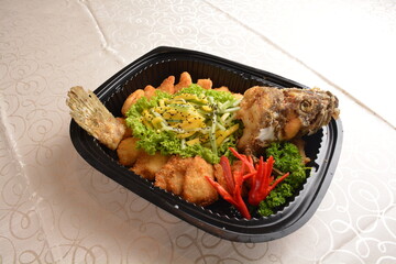 deep fried whole grouper fish with fresh Thai mango fruit salad and mango sauce in black party bento tray box for asian take away halal menu