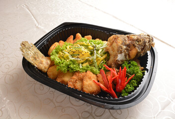 deep fried whole grouper fish with fresh Thai mango fruit salad and mango sauce in black party bento tray box for asian take away halal menu