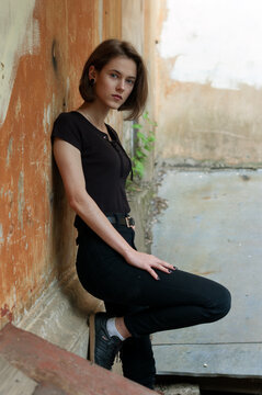 A brunette girl with a bob haircut in a black t-shirt stands in front of a textured wall 