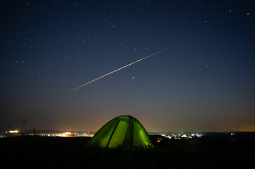 A tent outside the city among the fields at dawn, against the background of a falling meteorite © onyx124