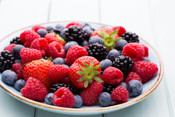 Fresh berry salad on blue dishes. Vintage wooden background.