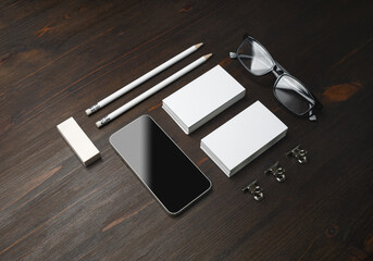 Smartphone and blank stationery: business cards, pencils, eraser and glasses on wood table background.