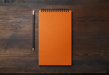 Blank orange notebook and pencil on wooden background. Stationery mock up. Flat lay. - Powered by Adobe