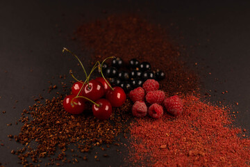 Fresh fruits and dried fruit powder. Cherry, currant, strawberry and raspberries  on dark paper...