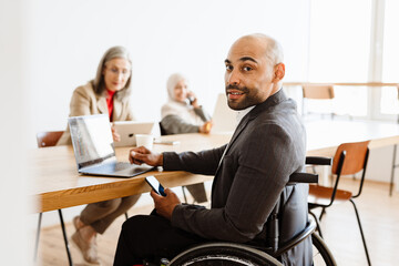 Unshaven man in wheelchair working with laptop and cellphone at office