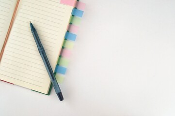 A notepad for writing with colored bookmarks and a pen on a white background. On the left side of...