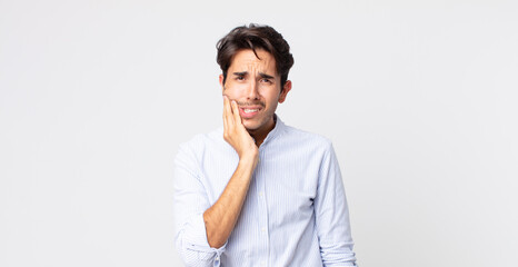 hispanic handsome man holding cheek and suffering painful toothache, feeling ill, miserable and...