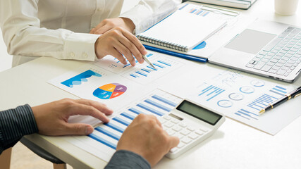 Picture of two young businessmen at a meeting Analyzing the financial markets, the youngster works in the office on his laptop while sitting at a wooden desk and analyzing the documents in hand. finan