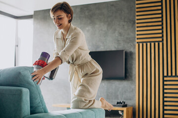 Young woman with rechargeable vacuum cleaner cleaning at home © Petro