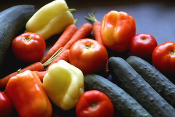 Zucchini, tomatoes, peppers, carrots and cucumbers on dark background. Selective focus.