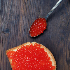 Still life with caviar. Photo of red caviar, sandwich and spoon on vintage wood table background. Top view. Flat lay.