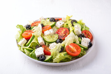Greek salad on a plate. Lettuce, tomatoes, cheese, cucumbers and olives.