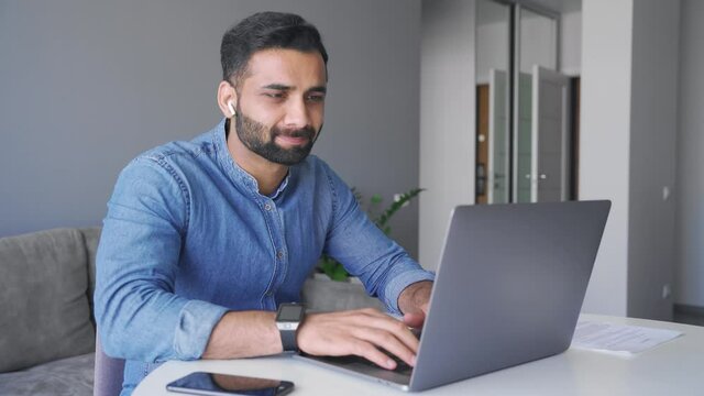 Young adult smiling indian businessman working on laptop computer at home office