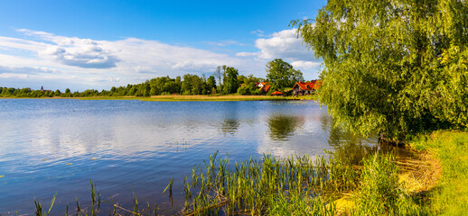 Panoramic summer view of Jezioro Selmet Wielki lake landscape with reeds and wooded shoreline in Sedki village in Masuria region of Poland - obrazy, fototapety, plakaty