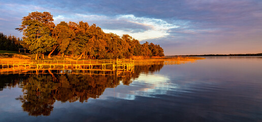 Panoramic summer sunset view of Jezioro Selmet Wielki lake landscape with vintage pier, reeds and wooded shoreline in Sedki village in Masuria region of Poland - obrazy, fototapety, plakaty
