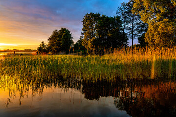 Fototapeta Panoramic summer sunset view of Jezioro Selmet Wielki lake landscape with vintage pier, reeds and wooded shoreline in Sedki village in Masuria region of Poland obraz