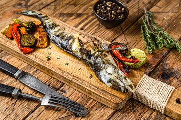 Grilled whole icefish with vegetables. Wooden background. Top view