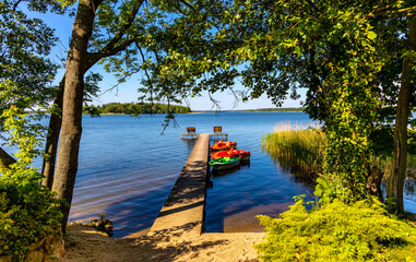 Panoramic summer view of Jezioro Selmet Wielki lake landscape with boat pier and wooded island in Sedki village in Masuria region of Poland