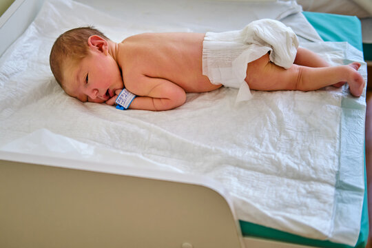 A newborn baby with a maternity hospital bracelet on his arm on a changing table