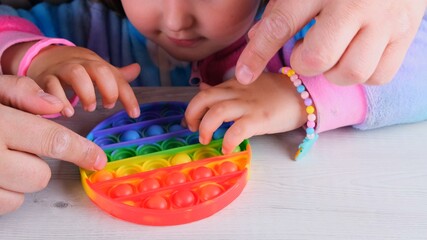 cute little girls play with dad with pop it sensory toy circle form. little female presses colorful...