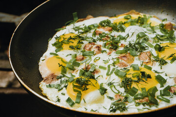 Close up of frying pan of fried eggs, bacon and organic greens, green grass on the background, cooked on the grill on a summer sunny day, summer breakfast, eating in nature 
