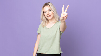 pretty albino woman smiling and looking happy, carefree and positive, gesturing victory or peace...
