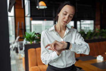 Serious elegant businesswoman checking time on wristwatch and waiting for meeting in cafe 