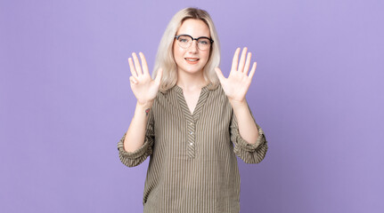pretty albino woman smiling and looking friendly, showing number nine or ninth with hand forward,...