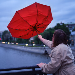 Adult woman with a red umbrella on the bridge in bad weather
