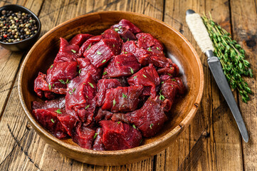Raw cut wild venison meat for a goulash in a wooden plate. Wooden background. Top view - obrazy, fototapety, plakaty
