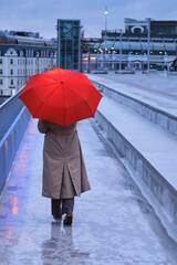 A woman with a red umbrella walks along a stone street in the light of evening lights