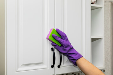 Hand in a purple rubber glove cleaning white kitchen cabinet