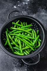 Raw green beans in a colander. Black background. top view