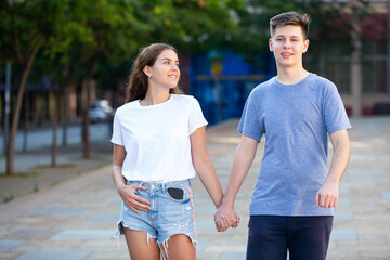 Young man and girl are walking on the street together and holding hands